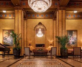 The dimly-lit luxury lobby at The Roosevelt New Orleans, complete with a chandelier and grand piano.