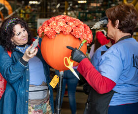 Two volunteers add orange and white flowers to a component of the 2024 Explore Louisiana Rose Parade float.