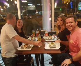 Four people smile at a table filled with trays of tacos, margaritas and beer.