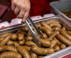 A hand uses tongs to serve links of boudin sausage from a steaming tray.
