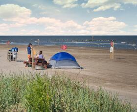 Tent pitched on the sandy beach at Grand Isle State Park near picnic tables and the Gulf shoreline.