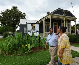 A couple walks past the River Road African American Museum sign in front of a charming historic building.