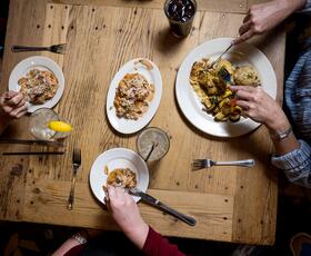 Diners share a meal at a wooden table, with plates of Southern-style dishes and drinks seen from above.