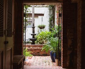 A view through an alleyway into a lush, brick-lined New Orleans courtyard with a fountain.