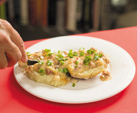 A golden buttermilk biscuit, cut in half, topped with gravy, green onions and flecks of black pepper.