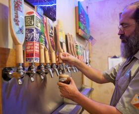 Bartender pouring a beer into glass from colorful taps at Bayou Teche Brewery in Arnaudville, Louisiana.