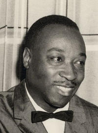 Musician Dave Bartholomew smiles and looks to his left while sitting in a chair in a tux