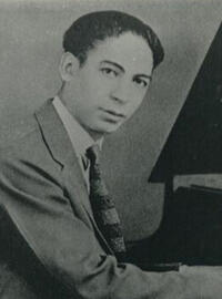 Jelly Roll looks at the camera while he plays the piano in a black-and-white picture
