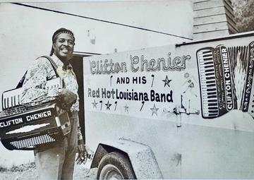 Clifton Chenier poses with an accordion in front of a vehicle with Clifton Chenier and his red hot Louisiana Band on it