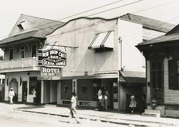 A black and white image of the exterior of the inn, with a sign reading "Dew Drop Inn"; a man crosses the street in front of it
