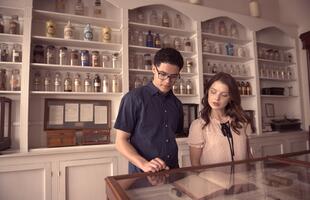 Two people examine medicinal artifacts at the New Orleans Pharmacy Museum, with a wall of bottles of various sizes and shapes behind them.