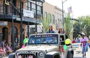 Two girls wearing crowns ride in a gray Jeep through the streets of downtown New Iberia during the Louisiana Sugar Cane Festival parade.