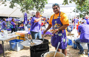 A man decked out in LSU Tigers merchandise stirs a large cast iron pot at a tailgate in Louisiana.