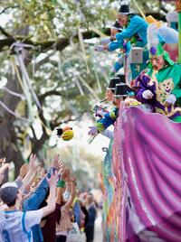 A crowed of parade goers reach out for Mardi Gras throws being tossed from a decorated and lively float.