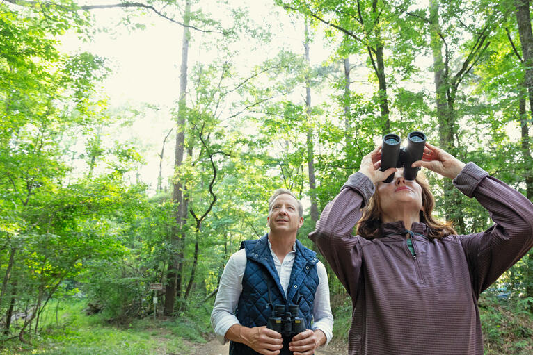 A couple hiking and the woman looking up through a binocular in a louisia astate park